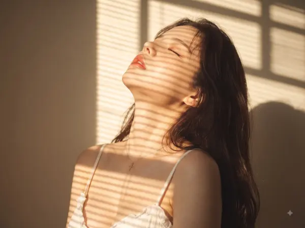 Woman with closed eyes enjoying sunlight on her face with shadows from window blinds.