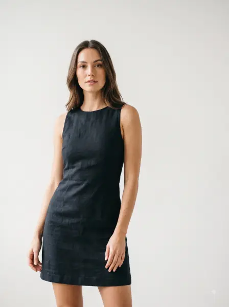Confident woman looking at the camera wearing a black sleeveless linen mini dress on a white background.